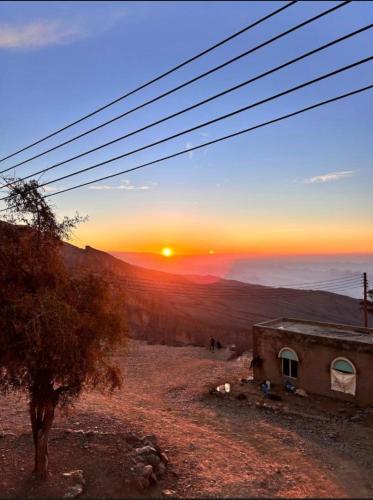 a sunset in the mountains with a building and a tree at Panorama Guest House Jabal Shams in Sa‘ab Banī Khamīs