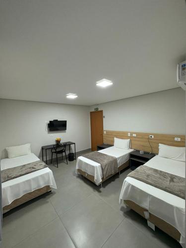 a room with three beds and a tv on the wall at Dicopi Hotel in Maringá