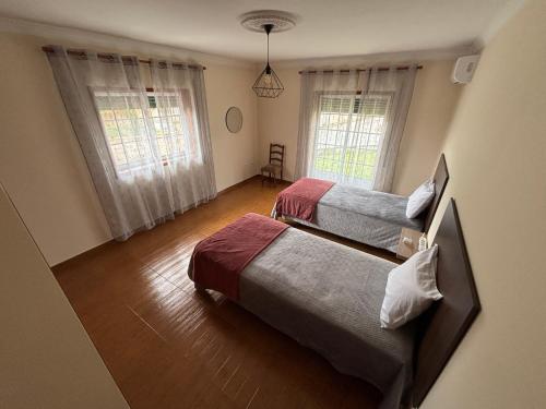 a bedroom with two beds and two windows at Casa dos Neto Carriço in Anadia