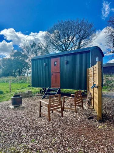 two wooden benches and a shed with a building at Cosy Shepherds Hut Lyme Regis, Cummins Farm in Bridport