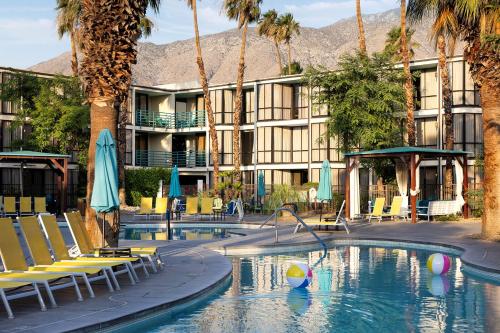 a hotel with a swimming pool with chairs and palm trees at Riviera Resort Palm Springs in Palm Springs