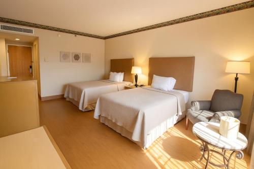 a hotel room with two beds and a chair at iStay Hotel Ciudad Victoria in Ciudad Victoria