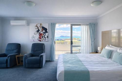 a bedroom with a bed and two chairs and a window at BKs Premier Motel Esplanade in Lower Hutt