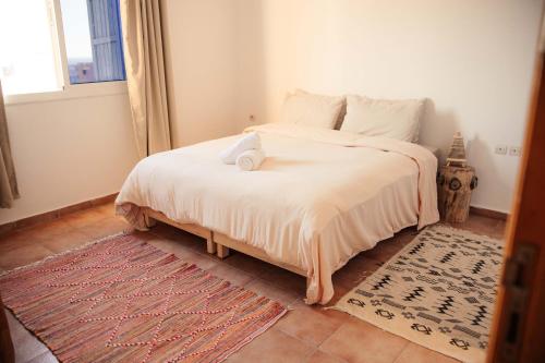 a bedroom with a bed with white sheets and a window at Get Salty Guesthouse in Tamraght Ouzdar