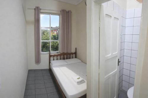a small white room with a bed and a window at Estação Pousada e Hostel in Cataguases