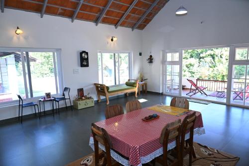 a living room with a table and chairs and windows at Whispering Meadows By Dazzle Destinations - Coorg in Somvārpet
