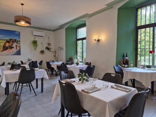 a dining room with white tables and chairs and windows at Logis Hôtel Restaurant Les Norias in Cazilhac