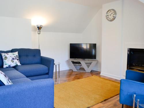 a living room with a blue couch and a tv at 3 Old Posting Stables in Gatehouse of Fleet