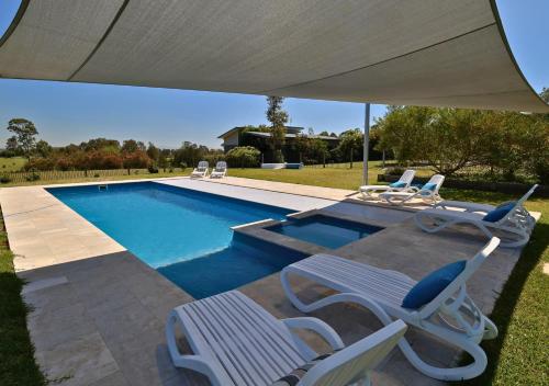 a swimming pool with chairs and an umbrella at Beltana Villas in Pokolbin