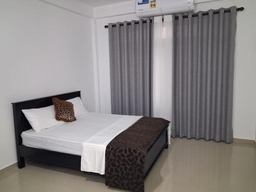 a bedroom with a bed with white sheets and curtains at Slayan properties in Mudungoda