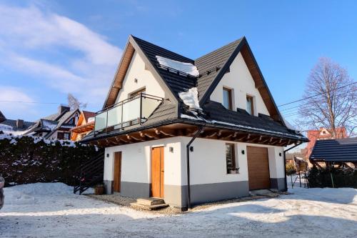 a house with a black roof in the snow at Pokoje KAMILA - Apartament 5 min pieszo do Kotelnicy in Białka Tatrzańska