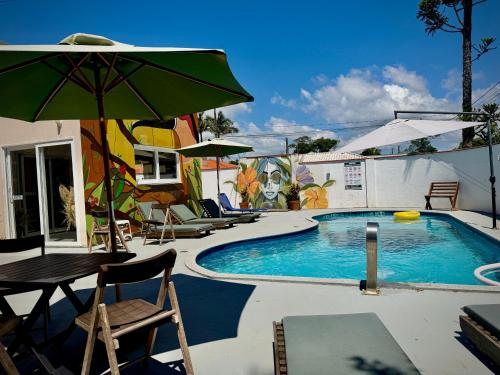 a pool with chairs and a table and an umbrella at Pousada Pássaros Park in Itapoa