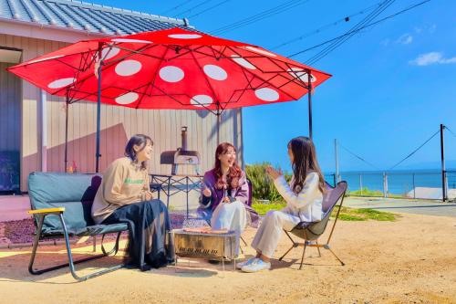 three women sitting in chairs under a red umbrella at 「淡路島一棟貸宿　野うさぎ 」高台から海を望む貸別荘！2023年新築離れの素泊まり in Noda