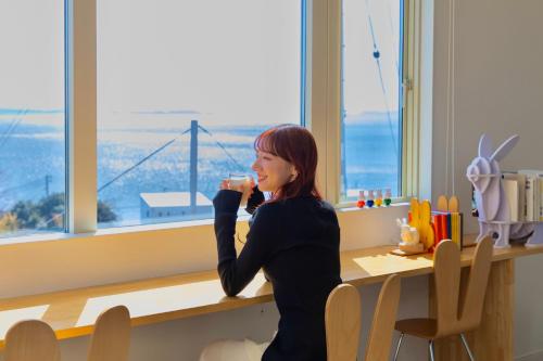 a woman drinking a cup of coffee in front of a window at 「淡路島一棟貸宿　野うさぎ 」高台から海を望む貸別荘！2023年新築離れの素泊まり in Noda