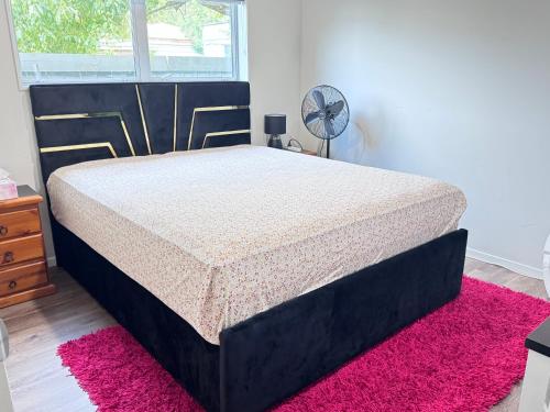 a black bed in a bedroom with a pink rug at Auckland City cozy Stay in Auckland