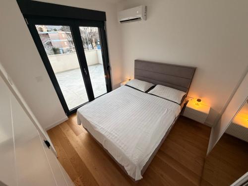 a bedroom with a white bed and a large window at Apartman TERRASSE in Trebinje