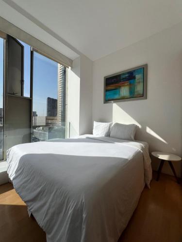 a white bedroom with a large bed and a window at Puerta Alameda Suites México in Mexico City