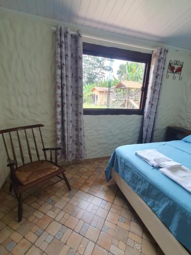 a bedroom with a bed and a chair and a window at Sossego Da Mata in Santo Antônio do Leite