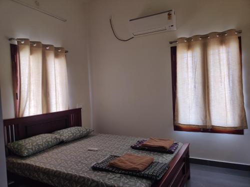 a bedroom with a bed and two windows at Wind Chimes in Tiruvannāmalai