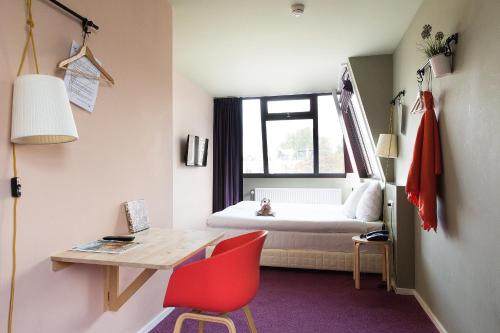 a room with a bed and a desk with a red chair at Hotel The Neighbour's Magnolia in Amsterdam