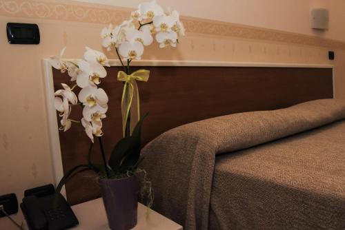 um vaso com flores brancas sobre uma mesa ao lado de uma cama em Albergo Munsci' em Rovello Porro