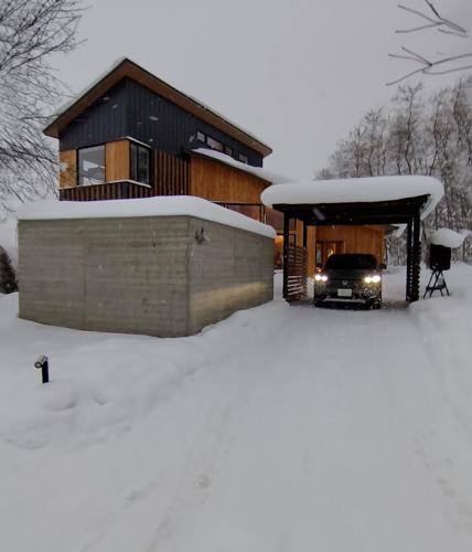 a house in the snow with a truck under it at Yama Sakura in Furano