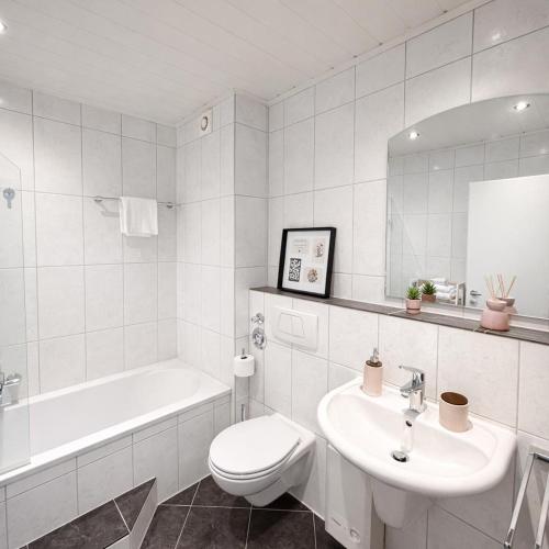 a white bathroom with a sink and a toilet and a tub at Penthouse mit Deisterblick & Balkon in Barsinghausen