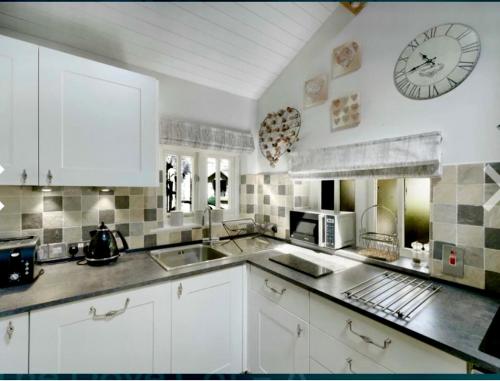a kitchen with white cabinets and a clock on the wall at Dove Cot country cottage Ambleside in Ambleside