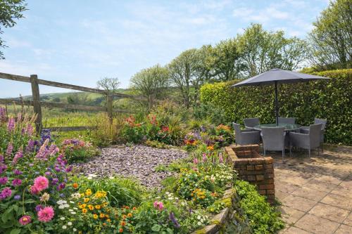 a garden with an umbrella and chairs and flowers at Coombe Corner Cornwall in Bude