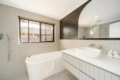 a bathroom with a tub and a sink and a mirror at 3BR Little Coastal Boho Home - Neverending Summer Fun near Themeparks & close to M1 exit in Pimpama
