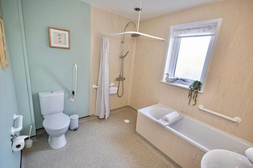 a bathroom with a toilet and a tub and a window at Owlswood Lodge in Orkney