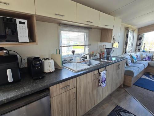 a kitchen with a sink and a living room at Seaside Caravan Home in Reighton