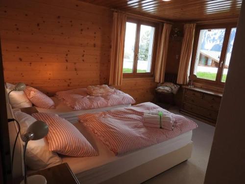 two beds in a wooden room with windows at Chalet Le Murier in Leysin