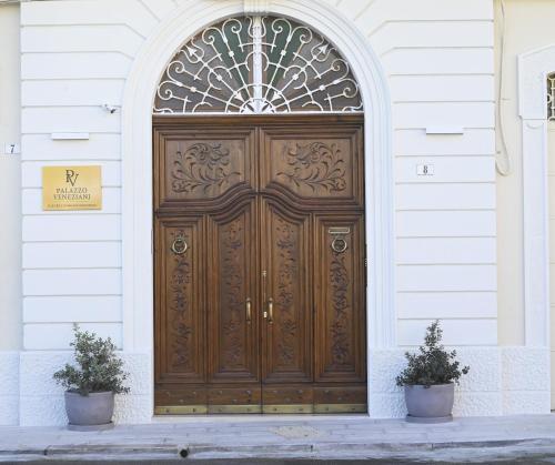 a large wooden door on a building with two plants at Palazzo Veneziani - Luxury Living in Monopoli in Monopoli