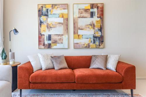 an orange couch in a living room with paintings on the wall at Elite LUX Holiday Homes - Serene Golf View Living 1 BHK in Damac Hills, Dubai in Dubai