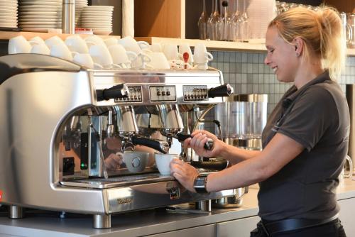 a woman preparing a cup of coffee in a kitchen at Steverbett Hotel in Lüdinghausen