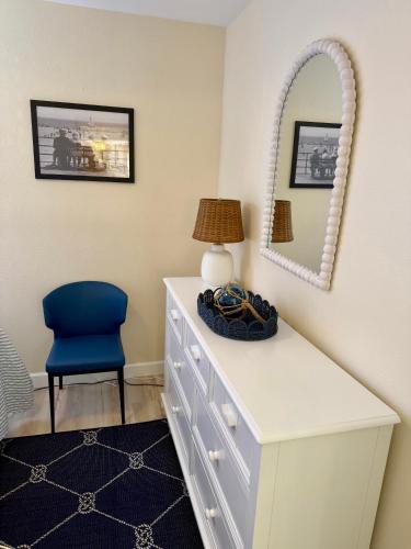 a white dresser with a blue chair and a mirror at Birdsong Beachfront Condo in St. Pete Beach