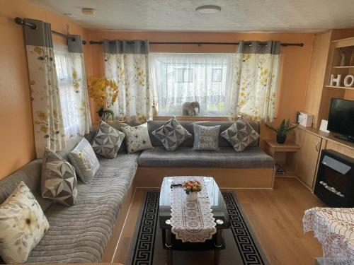 a living room with a couch and a table at Bright Family Caravan with Deck & BBQ at Seawick Holiday Park, Clacton in Clacton-on-Sea