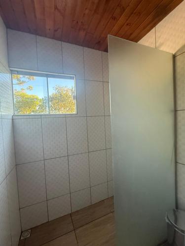 a bathroom with white tiled walls and a window at Chácara pontarolo in Guarapuava