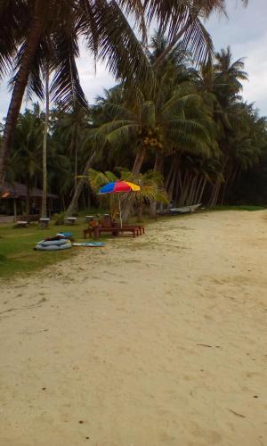 a beach with tables and umbrellas and palm trees at Happy Days Resort in Ko Mak