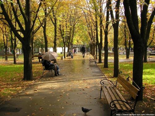 a person sitting on a bench with an umbrella in a park at Apartment in the center on Spasskaya Street in Mykolaiv