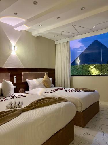 two beds in a hotel room with a large window at Glow Pyramids View Hotel in Cairo