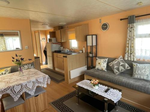 a living room with a couch and a table at Bright Family Caravan with Deck & BBQ at Seawick Holiday Park, Clacton in Clacton-on-Sea