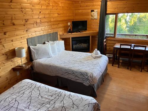 a bedroom with two beds and a fireplace in a log cabin at Bear Cove Cottages in Port Hardy