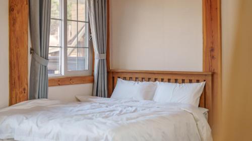 a bed with white sheets and a window at Daecheon Ocean Forest Pension in Boryeong