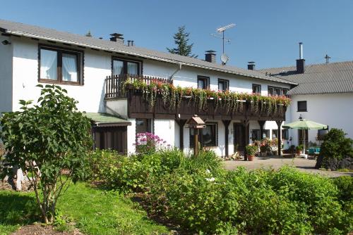 ein weißes Gebäude mit einem Balkon mit Blumen darauf in der Unterkunft Pension Haus Liesertal in Üdersdorf