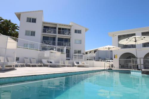 a pool with chairs and umbrellas next to a building at Don Pancho Beach Resort in Bargara