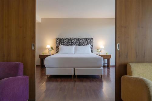 a bedroom with a white bed and two chairs at NH Córdoba Panorama in Córdoba