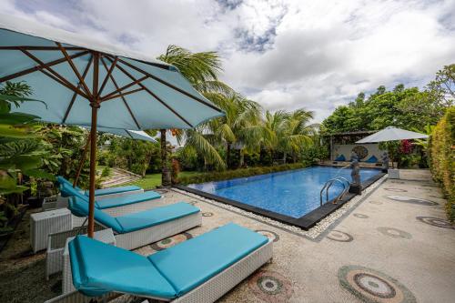 a pool with blue lounge chairs and an umbrella at Cove Jiwana Villa in Nusa Dua