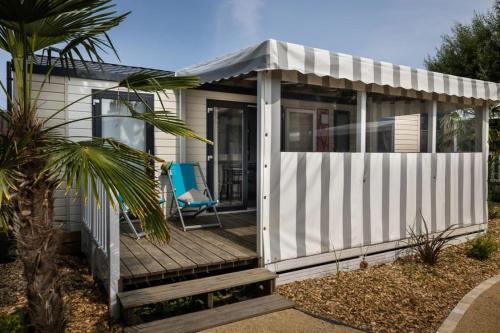 a white shed with a chair on a wooden deck at ZEcamping 4 étoiles animé piscine couverte 1km plage fitness mobil-home TV in Saint-Jean-de-Monts